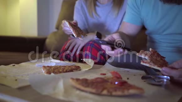 几个男人和女人晚上在客厅的沙发上吃披萨同时在电视上看电影概念视频的预览图