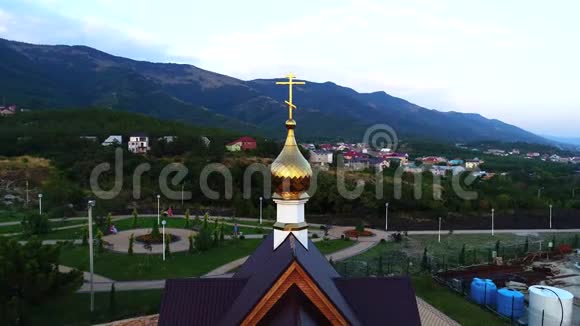 在黄昏时分绕着一座小东正教教堂的镀金穹顶飞行背景中的山脉视频的预览图