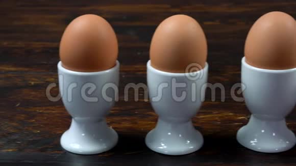 在蛋杯中的蛋杯中一排煮鸡蛋对着一个带条纹的蛋杯中的单个鸡蛋微笑着视频的预览图