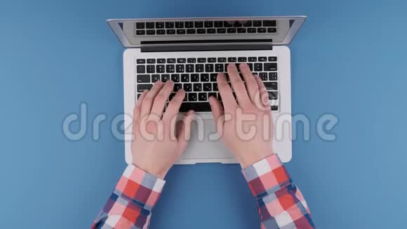 双手在蓝色背景上的笔记本电脑键盘上打字上景视频的预览图