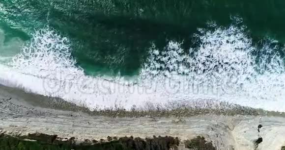 海浪与白色泡沫翻滚在一个高岩石岸下的一个摇摇欲坠的海滩从宝座上俯瞰视频的预览图