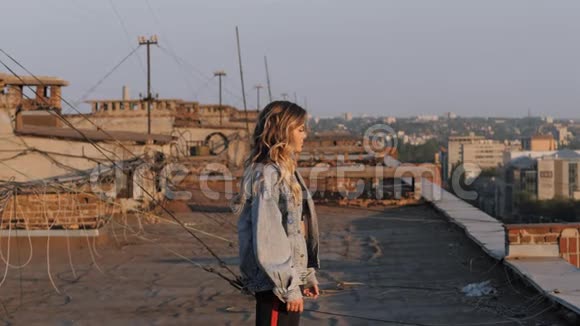 日落时分一个老房子屋顶上的女孩欣赏从高处俯瞰城市的景色视频的预览图
