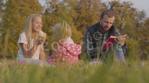 留着胡子的白种人在户外给他可爱的女儿用红色封面重订书漂亮的少年金发的小女孩视频的预览图