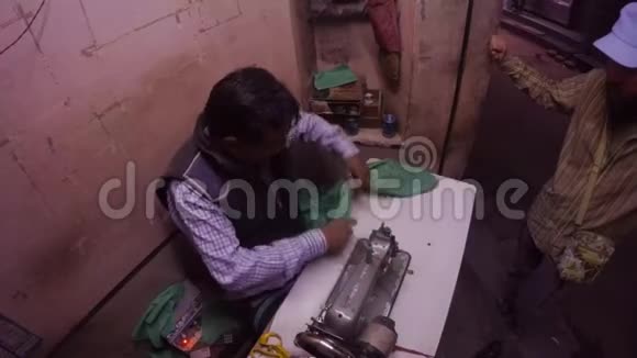 印度裁缝在老式缝纫机上用绿色布料工作客户站在街道上背景是摩托车视频的预览图