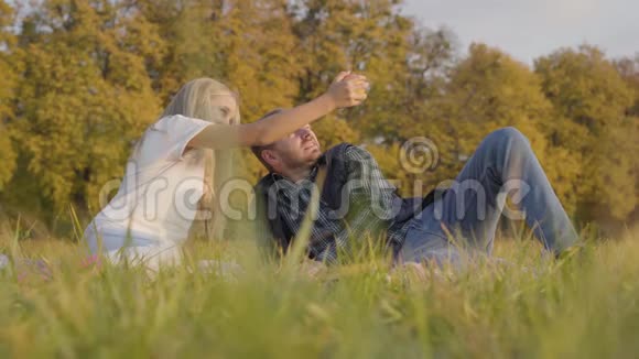 父亲和女儿坐在秋天的草地上为苹果而战白人男子和年轻的金发女孩视频的预览图