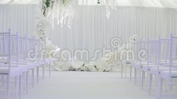 宽敞的白色婚礼房有一个大的婚礼可爱花环新娘和新郎在它下面白色椅子视频的预览图