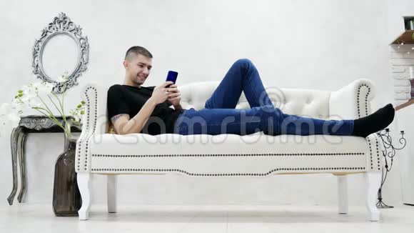 年轻人在沙发上放松在现代的房子里使用智能手机玩手机视频的预览图