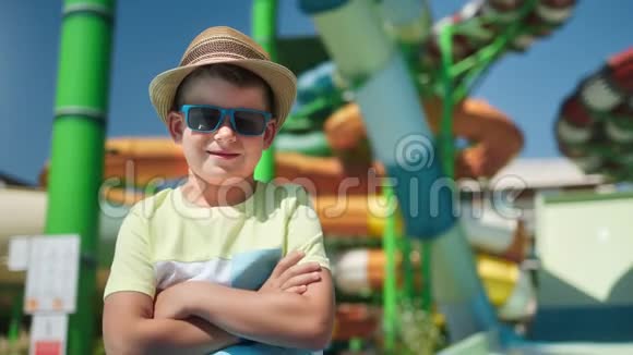 戴着太阳镜戴着帽子的时髦可爱男孩在露天水上乐园的背景下微笑视频的预览图