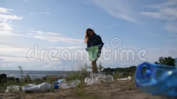 一个年轻的女人打扫海滨塑料瓶盘子和用具散落在整个土地上4K慢慢视频的预览图