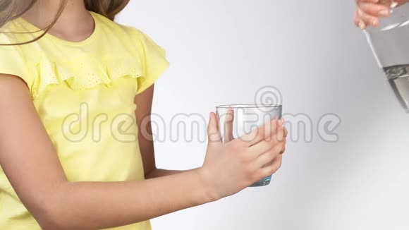 妈妈把水倒进一个小女孩杯子里小女孩把水倒进玻璃杯里一个穿着白色黄色裙子的女孩视频的预览图