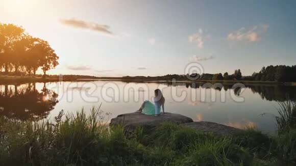 一个孤独的女孩坐在湖边在日落时泼水录像在移动视频的预览图