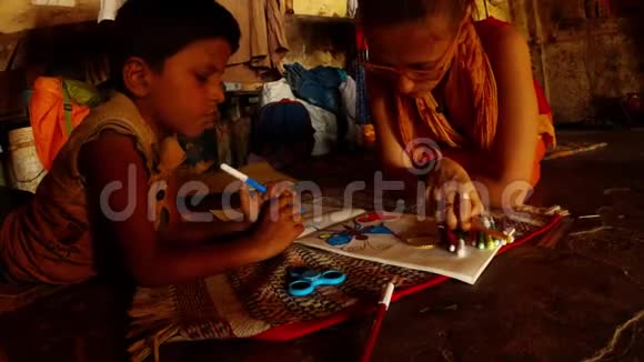 在瓦拉纳西贫民区肮脏破旧的房间里的一堆衣服里一个白人妇女和一个印度小男孩用毛毡尖笔画画视频的预览图