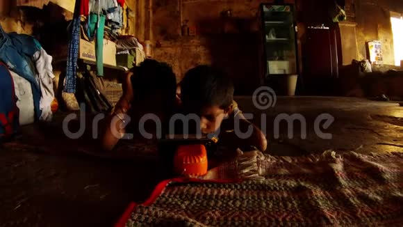两个印度男孩躺在地板上看着电话里的一堆衣服干的肮脏的破旧的墙瓦拉纳西的贫民窟视频的预览图