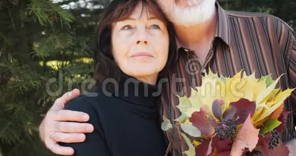 快乐的老夫妇喜欢在秋天的松树下拥抱慢动作视频的预览图