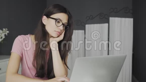 戴眼镜的漂亮学生在家学习笔记本电脑视频的预览图