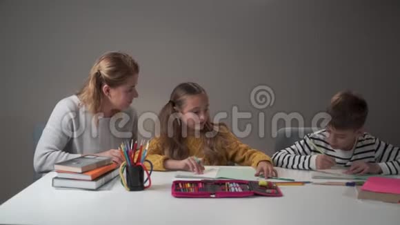 两名白人儿童和年轻女教师坐在桌子旁交谈的肖像教师教孩子们视频的预览图