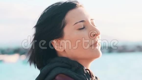 一个自然的黑发女人的形象没有化妆享受微风和阳光眼睛紧闭在海边视频的预览图