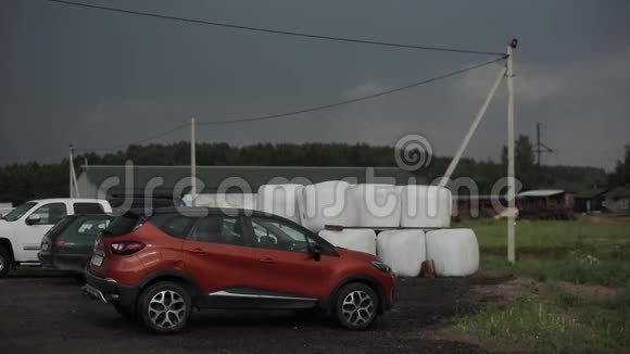 雷雨前几辆汽车停在建筑物附近的农村逆着黑暗的天空视频的预览图