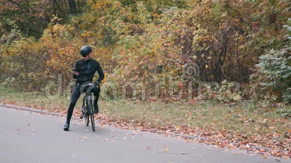 年轻的有动力的职业自行车骑着自行车站在秋季公园打电话留言黑人运动中的男运动员视频的预览图