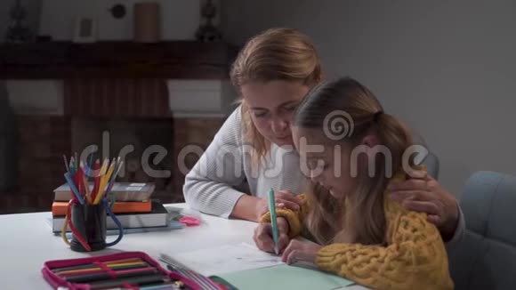快乐的白种人母亲看着她可爱的小女儿做作业微笑着拥抱着她小聪明的女孩视频的预览图
