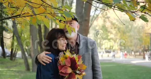 快乐的老夫妇拥抱着享受秋天在一个舒适的公园里的树木慢动作视频的预览图