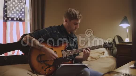 年轻男子坐在床上放松和练习在家里弹声吉他一个真正的吉他手视频的预览图