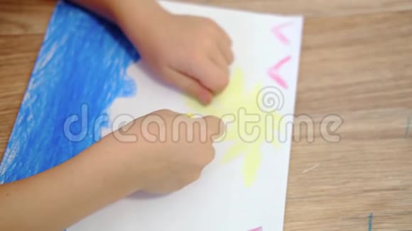 4k家里的孩子两手合拢一个金发的小孩子在地上画着黄色的太阳和蓝色的大海视频的预览图