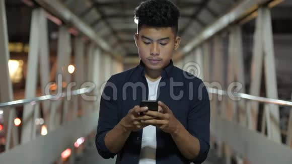 快乐的亚洲年轻人晚上在天桥上用电话视频的预览图