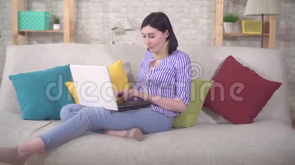 年轻女子坐在沙发上脖子上戴着项圈用笔记本电脑视频的预览图