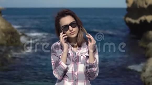 一个年轻的女人在大海的背景下打电话给智能手机有电话的女人在度假蓝色的大海视频的预览图