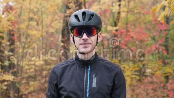 秋季公园年轻职业男性自行车运动员肖像迷人的微笑活泼的家伙摘下黑色头盔和眼镜视频的预览图