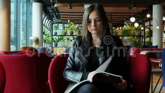 美丽的女人在现代咖啡馆等着看杂志视频的预览图