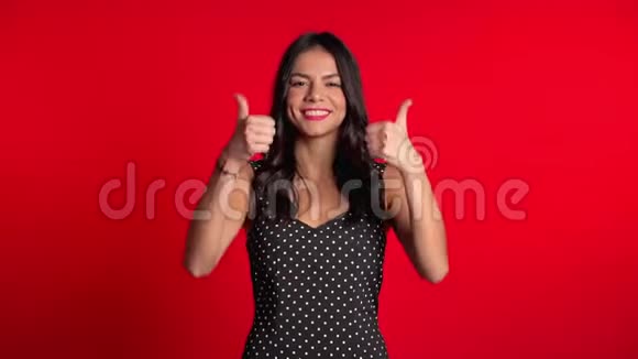 年轻的拉丁女人穿着完美的妆容竖起大拇指在红色上签名视频的预览图