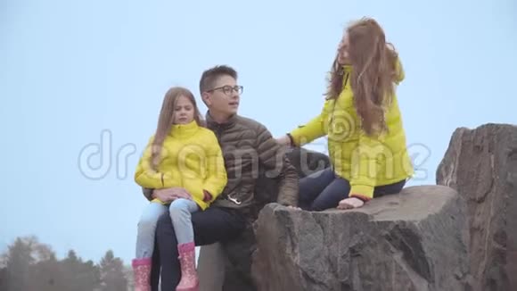 哥哥和姐姐和他们的年轻母亲在秋天公园里坐在岩石上交谈布莱克杜伯曼来了视频的预览图