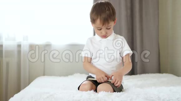 一个小男孩的肖像孩子坐在床上玩智能手机视频的预览图