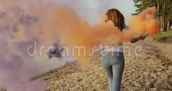 一个长着雀斑的红发女孩带着紫色和橙色的五颜六色的烟雾在河岸上奔跑视频的预览图