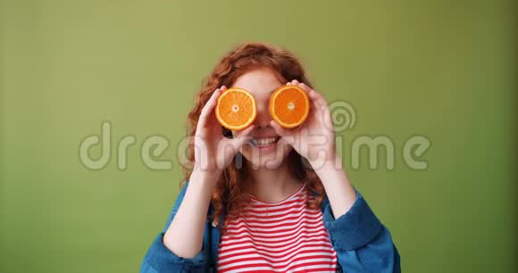 一个漂亮的女孩拿着新鲜的橘子靠近她的眼睛微笑着绿色的背景视频的预览图