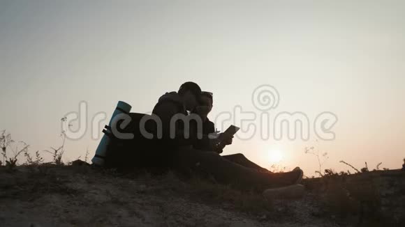 日落时一对年轻的游客坐在山顶上享受一块石碑视频的预览图