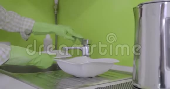 成熟的女人戴着橡胶手套用海绵和洗涤剂在厨房洗碗视频的预览图