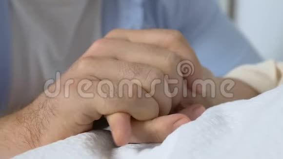 年轻男子握着老妇人的手感到极度担忧快要死去的母亲视频的预览图