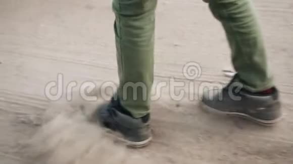 一个男孩走在沙地上用脚踢灰尘视频的预览图
