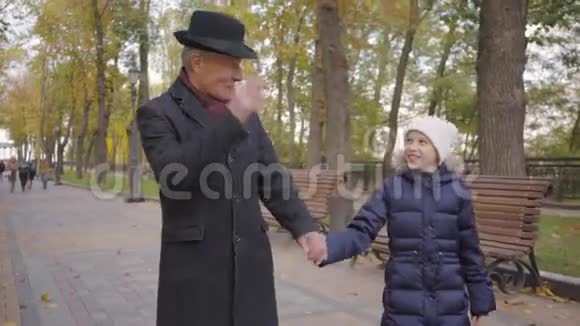穿着优雅的黑色帽子和外套的高加索人和孙女在秋天公园的小巷里散步视频的预览图