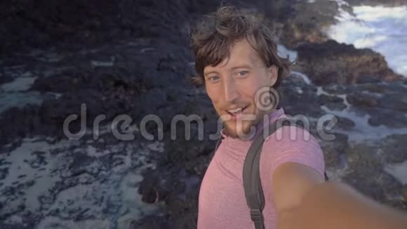 年轻人在黑色火山海滩上制作自拍视频波浪在岩石上撞击造成自然的外观视频的预览图