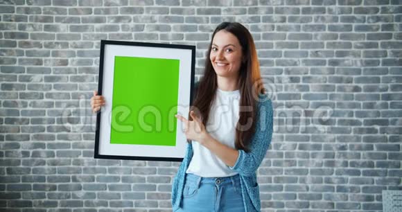 女孩指向绿色屏幕图片的肖像显示拇指向上的微笑视频的预览图