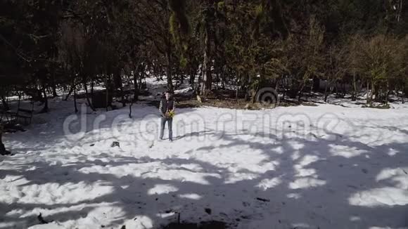 穿着格子衬衫和背心的人在森林里的一片白雪皑皑的草地中间扔出一束春天的美洲狮视频的预览图