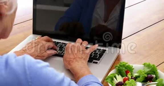 把成熟的女人用笔记本电脑把沙拉放在桌子上视频的预览图