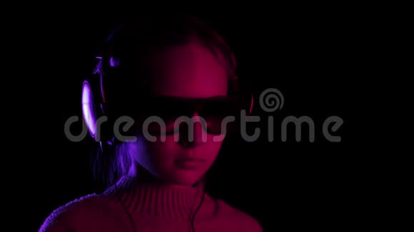 十几岁的女孩在红色和蓝色灯光的黑暗工作室里戴着耳机唱歌跳舞听音乐的年轻女孩视频的预览图