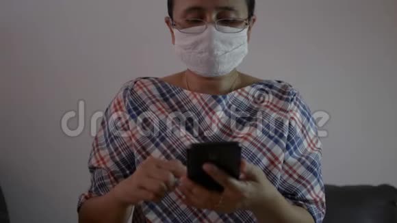 女士戴着防护面罩使用手机智能手机在客厅的社交网络上进行交流视频的预览图