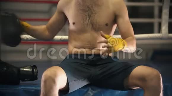 拳击训练一名纹身男子坐在拳击台上戴上拳击手套视频的预览图