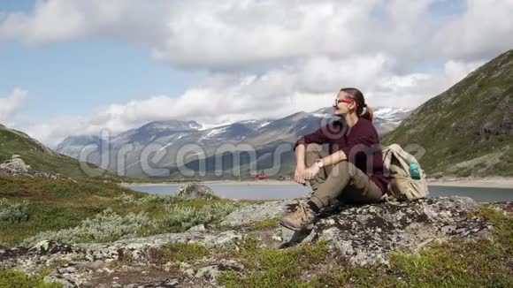 年轻的女旅行者穿着徒步旅行的靴子坐在岩石上视频的预览图